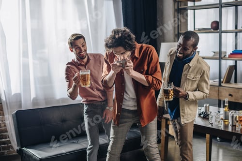 Preview: laughing male friends looking at man drinking beer from can
