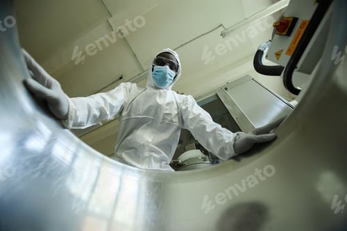 Preview: Low angle of black man wearing protective suit looking in tank at factory
