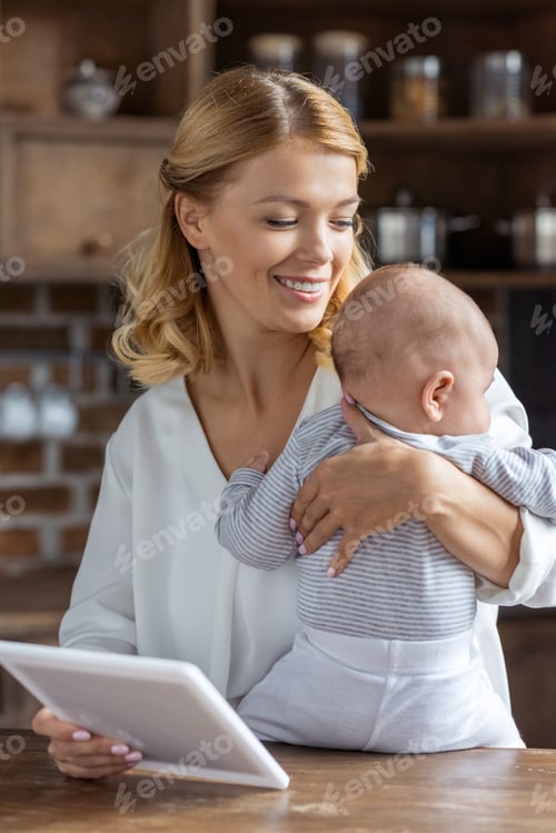 Preview: portrait of smiling mother holding infant and photo frame in hands at home