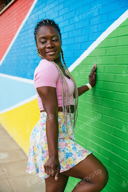Preview: A woman in a pink shirt and floral skirt poses in front of a green wall