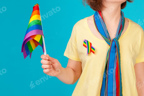 Preview: Young unrecognizable woman holding small LGBT flag on bright color background