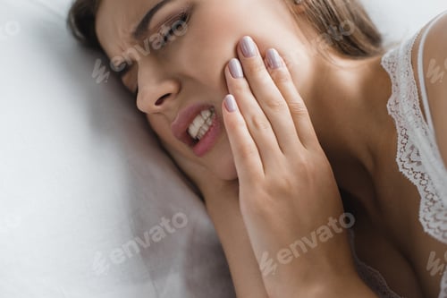 Preview: close-up view of young woman suffering from toothache while lying in bed