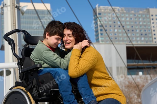 Preview: Happy mother hugging her son with cerebral palsy in wheelchair outdoors