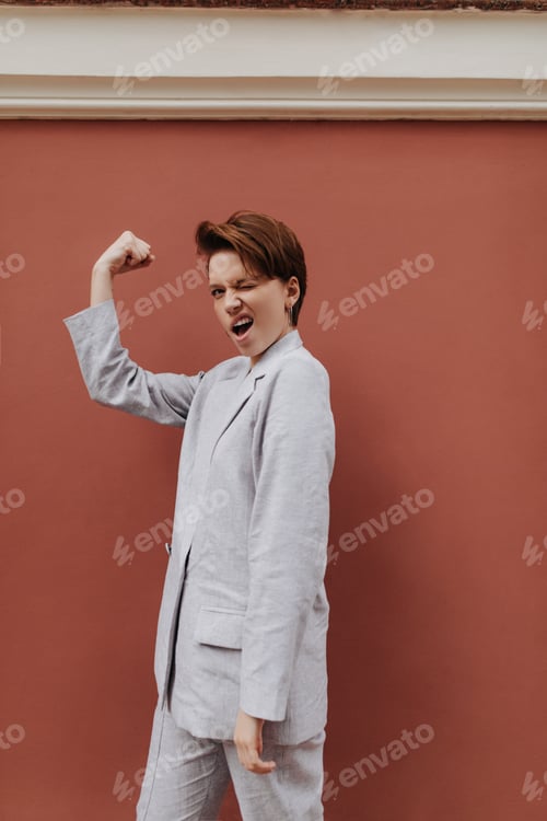 Preview: Cheerful woman in grey suit showing her power. Short-haired girl in oversize jacket and pants demon
