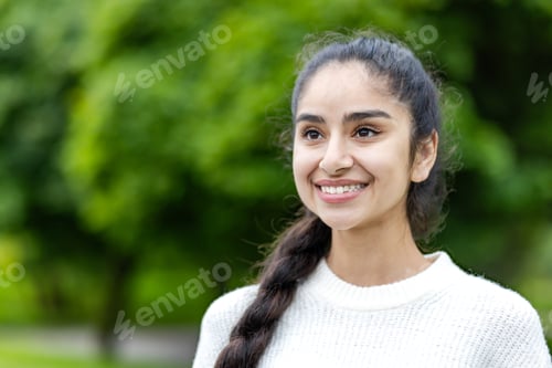 Preview: Close-up photo of a happy young Indian woman standing outside the park, smiling, dreamy and