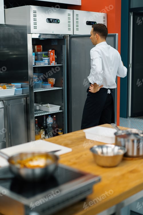 Preview: professional kitchen chef looks into the fridge and chooses ingredients for cooking food concept