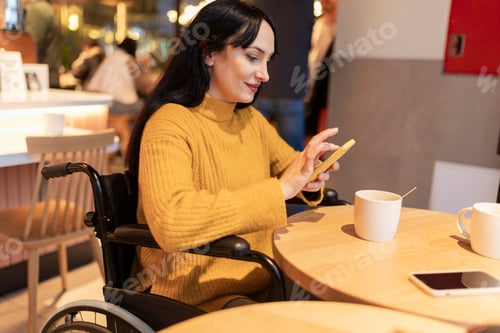 Preview: Smiling woman in wheelchair using smartphone in cafe