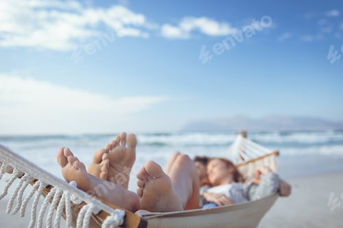 Preview: Front view of relaxed Caucasian couple sleeping on hammock at beach on sunny day