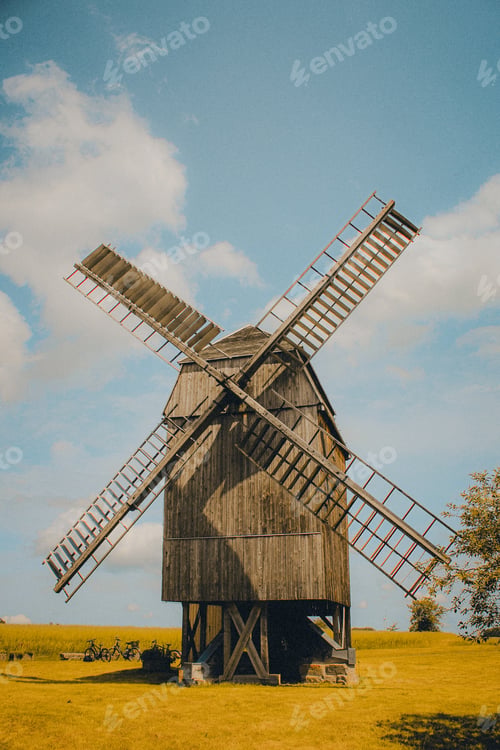 Preview: Windmill stands near a lush green field, with trees in the background.