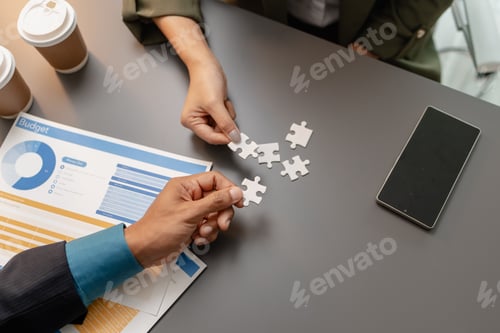 Preview: Business people holding puzzle pieces together on the office desk, symbolizing teamwork
