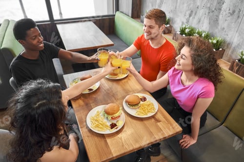 Preview: Group of friends sitting in cafe at table, clinking glasses