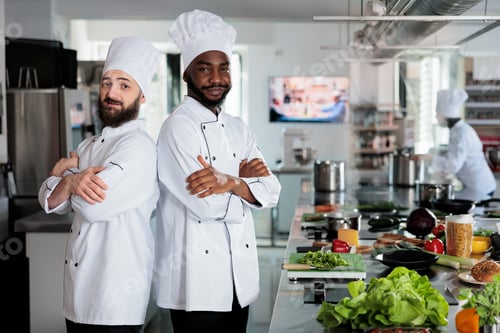 Preview: Multiethnic male cooks standing in restaurant professional kitchen with arms crossed while preparing