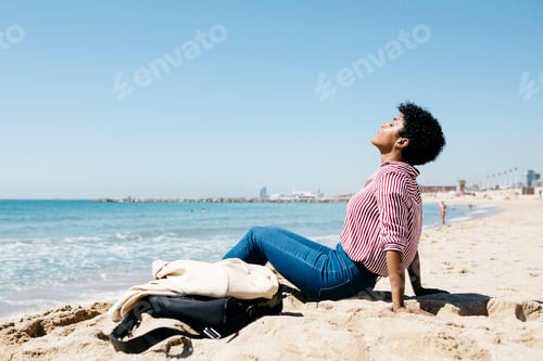 Preview: Woman sitting on the beach enjoying the sun after work