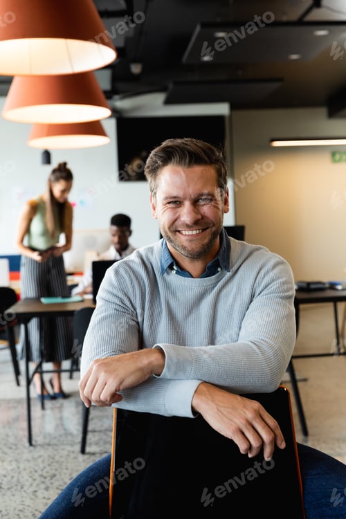 Preview: Portrait of smiling caucasian mid adult businessman sitting on chair in creative office