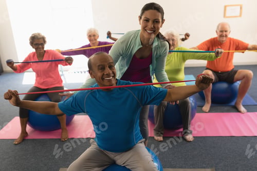 Preview: Front view of happy young female trainer assisting senior man in fitness studio