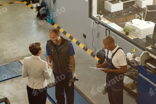 Preview: Above view of happy mechanic greeting a businesswoman in a repair shop.