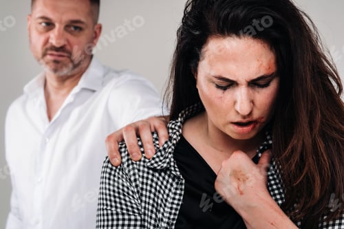 Preview: A woman beaten by her husband standing behind her and looking at her aggressively. Domestic violence