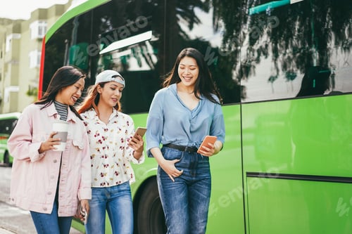 Preview: Happy young asian friends using mobile phones at bus station - Focus on center girl face
