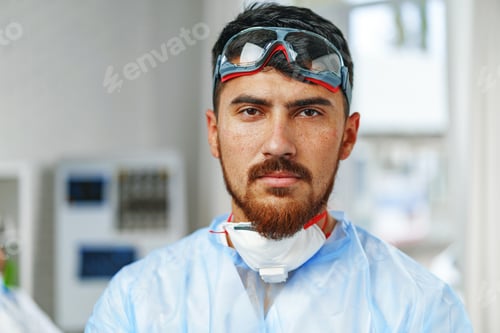Preview: Male doctor in protective medical gown standing in hospital cabinet