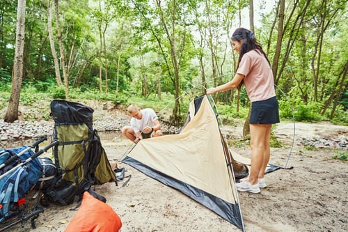 Preview: Happy sporty couple preparing camp near stream
