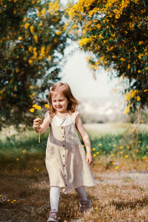 Preview: Toddler little girl walking outside in spring park with blooming trees, holding yellow fresh flowers
