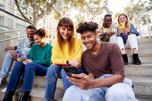 Preview: Multiracial group of young friends sitting on stairs hanging out, using mobile phones.