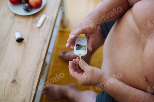 Preview: Overweight man checking blood glucose level at home using a fingerstick glucose meter.