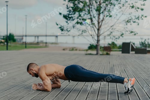 Preview: Sporty man stands in plank pose, practices yoga and dressed in active wear, breathes fresh air