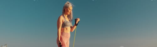 Preview: Woman in sportswear exercising on the sports site, using rubber bands