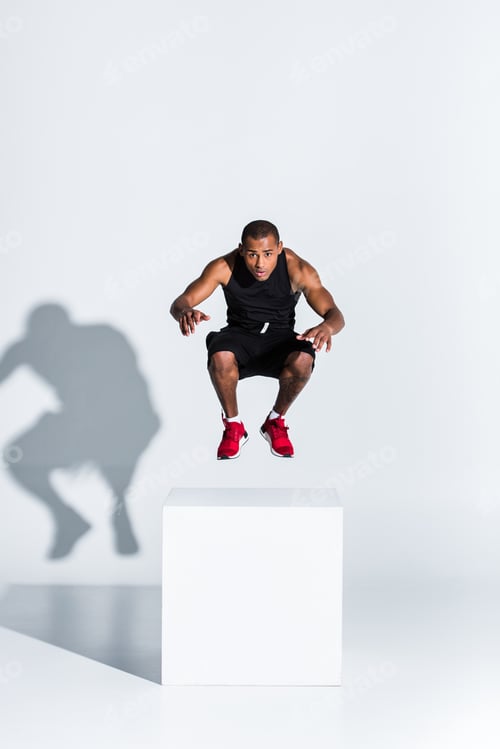 Preview: young african american sportsman jumping and looking at camera on grey