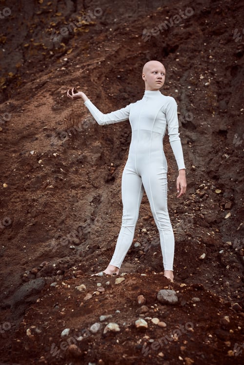 Preview: Full length portrait of young hairless girl with alopecia in white suit holding handful of earth