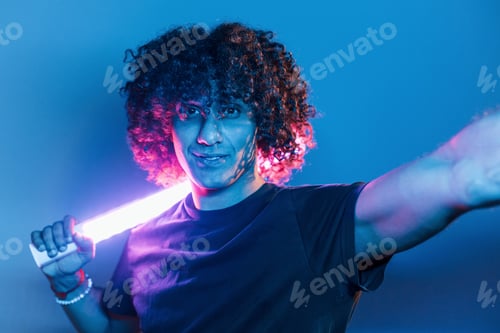 Preview: Young beautiful man with curly hair is indoors in the studio with neon lighting