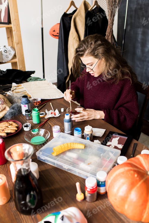 Preview: Busy girl in glasses mixing paints in workshop