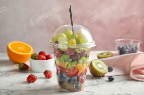 Preview: Fresh tasty fruit salad in plastic cup on white marble table