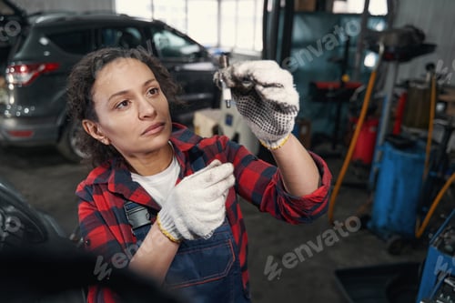 Preview: Female auto mechanic checking car part in automobile garage
