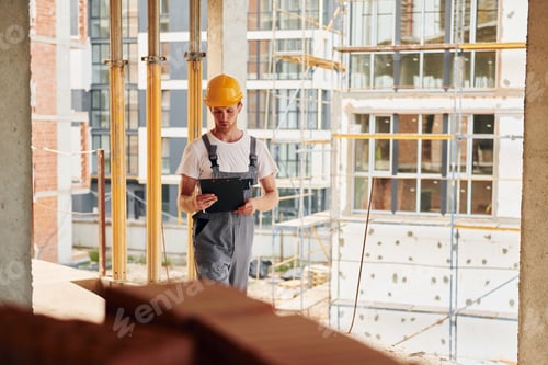 Preview: Yellow colored hard hat. Young man working in uniform at construction at daytime