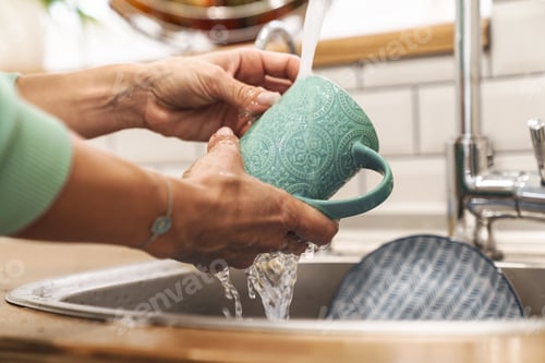 Preview: Woman indoors at home wash the dishes at the kitchen.