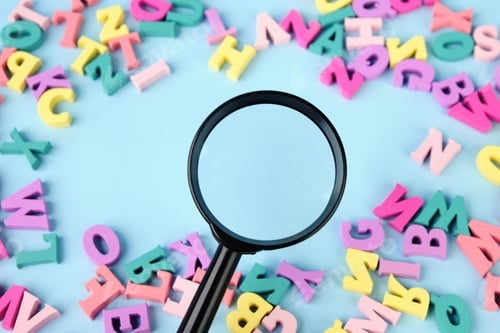 Preview: Lots of multicolored wooden letters scattered on a blue background. Magnifying glass in center.