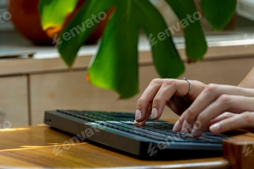 Preview: Person typing on a black wireless keyboard on a wooden table in daytime sunlight