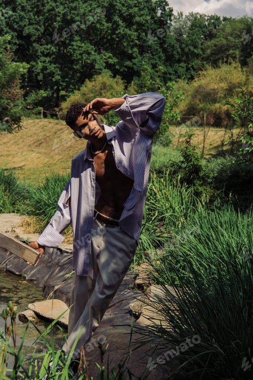 Preview: stylish african american man with hand near face posing near pond in park