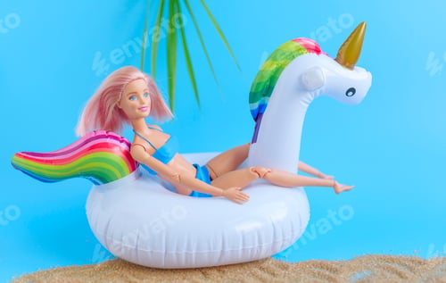 Preview: Barbie doll in swimsuit having rest on inflatable swan unicorn on the sea cost