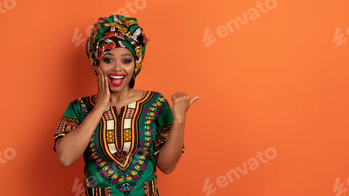 Preview: Amazed black woman in african clothes showing copy space