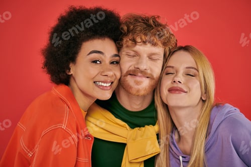 Preview: polyamorous concept, portrait of young man and multicultural women on coral background, studio shot,