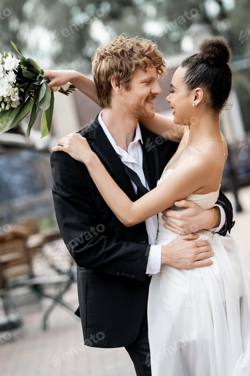 Preview: interracial newlyweds in elegant attire embracing on street, outdoors wedding, banner