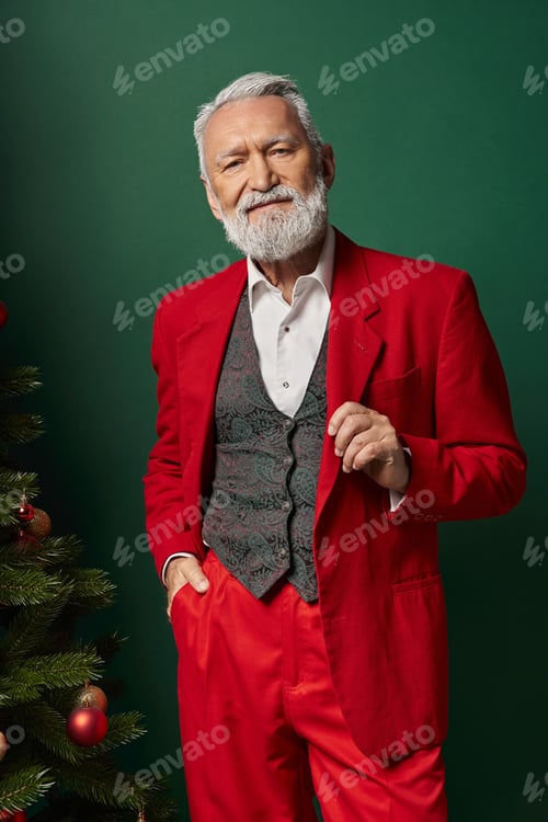 Preview: stylish Santa with white beard wearing classy suit and posing next to pine tree, winter concept