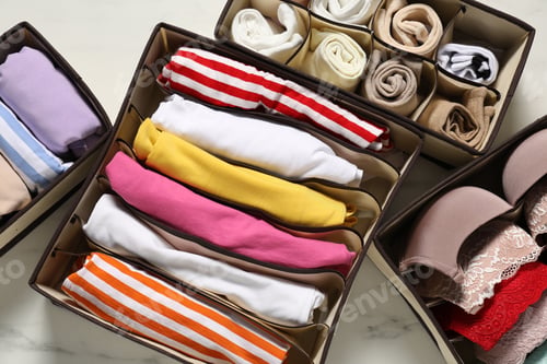 Preview: Organizers with folded clothes and underwear on white marble table, flat lay