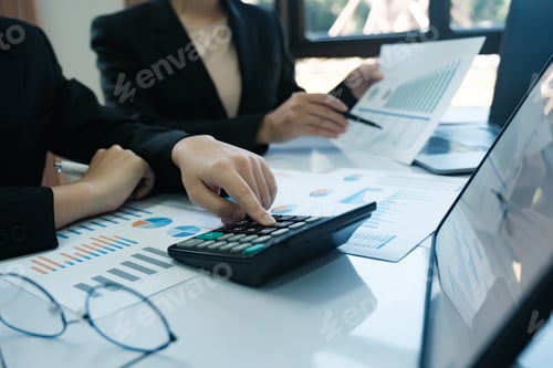 Preview: A woman is using a calculator to add numbers on a table with other people