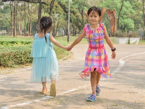 Preview: Two little sisters holding each other hands in a summer green park.