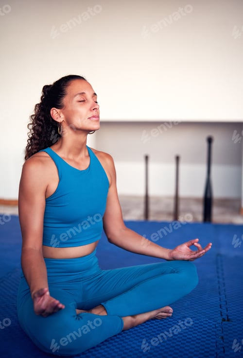 Preview: mid adult latina woman sitting in lotus position meditating indoors