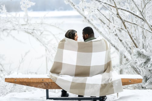 Preview: a mixed couple in love sits on a bench in winter. there is a lot of snow around them